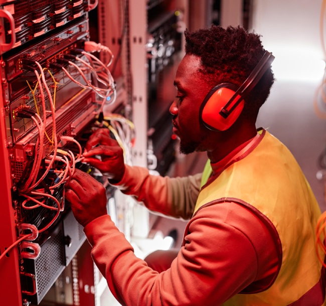 A man in a yellow vest and headphones is working on a server in a tech environment.