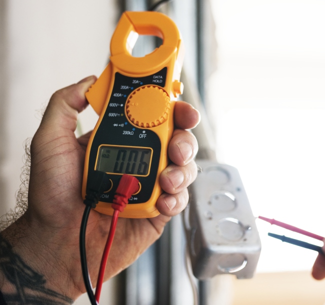 A person holding a digital multimeter in their hand, ready to measure electrical values.