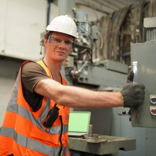 A man wearing an orange vest and hard hat stands, ready for work at a construction site.